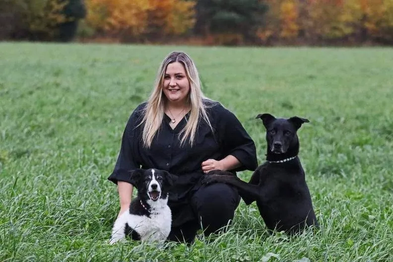 Katrin kniet mit zwei Hunden in einer Wiese