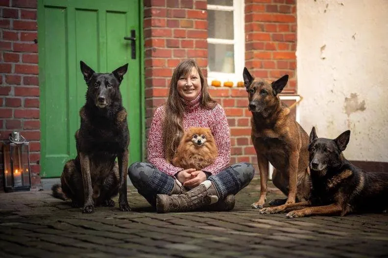 Lynn sitzt mit ihren vier Hunden vor einer grünen Tür