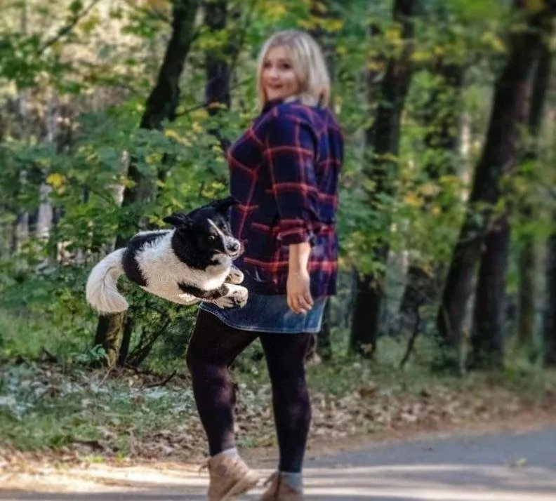 Border Collie springt neben einer Frau durch den Wald